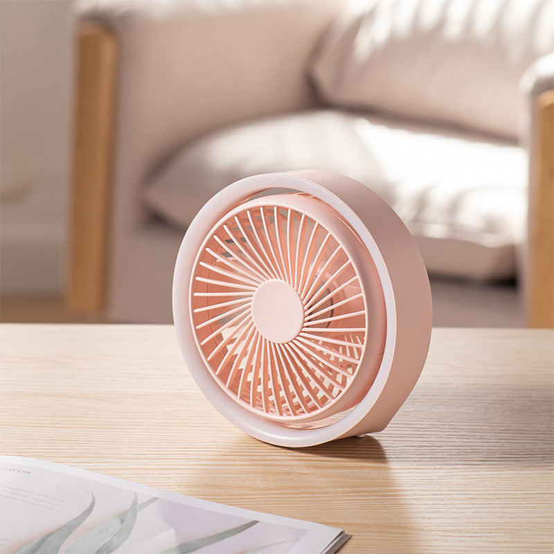 Pink and white portable fan on a wooden table with a blurred background