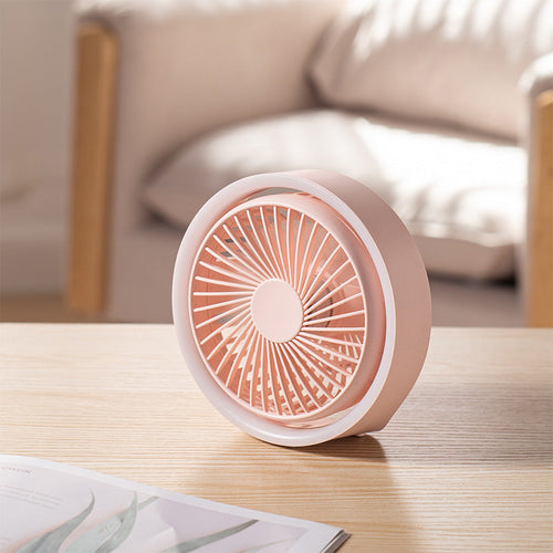 Pink and white portable fan on a wooden table with a blurred background